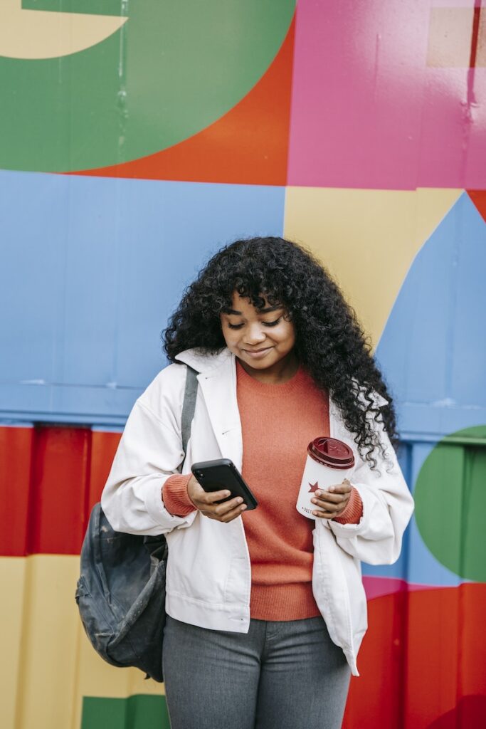Smiling black woman using smartphone near colorful wall